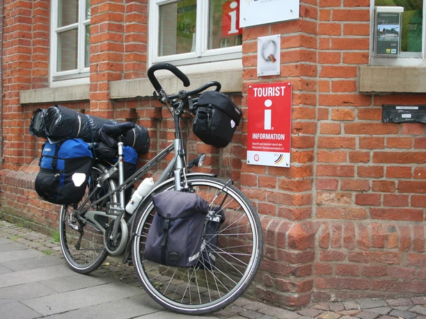 A loaded bicycle leans against the red brick building of the Nienburg Tourist Information Office.