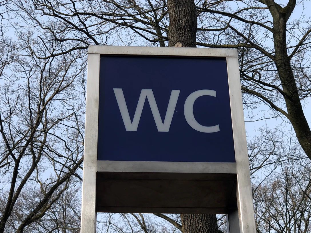 WC Öffentliche Toilette in einem parkähnlichen Gebiet, umgeben von Bäumen, unter freiem Himmel.
