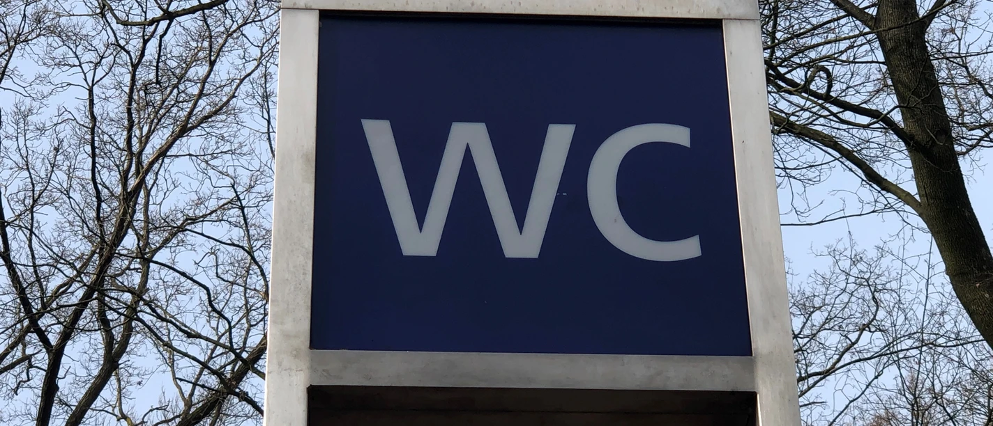 WC Öffentliche Toilette in einem parkähnlichen Gebiet, umgeben von Bäumen, unter freiem Himmel.