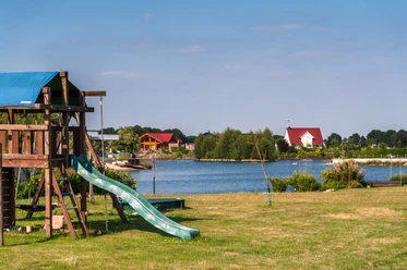 Lünner See Grüne Wiese mit Spielgerüst und Rutsche am Ufer des Lünner Sees unter blauem Himmel.
