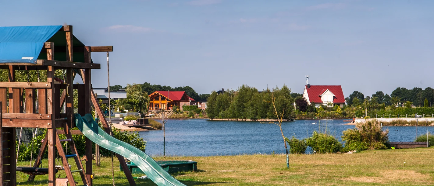 Lünner See Grüne Wiese mit Spielgerüst und Rutsche am Ufer des Lünner Sees unter blauem Himmel.