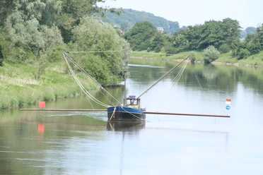 Aalschokker Landesbergen Een traditionele palingaak op een rustige rivier, omringd door groene bomen en glooiende heuvels.