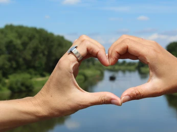 Aalschokker Landesbergen Zwei Hände formen ein Herz vor einer Flusslandschaft, mit Bäumen und blauem Himmel im Hintergrund.Two hands form a heart in front of a river landscape, with trees and blue sky in the background.To hænder danner et hjerte foran et flodlandskab med træer og en blå himmel i baggrunden.Twee handen vormen een hart voor een rivierlandschap met bomen en een blauwe lucht op de achtergrond.