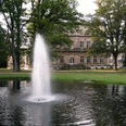 Palaisgarten Brunnen mit sprudelndem Wasser vor einem historischen Gebäude, umgeben von grünen, großen Bäumen.