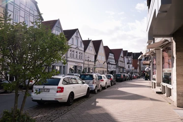 Krumme Straße Straßenansicht mit parkenden Autos und traditionellen Fachwerkhäusern unter wolkigem Himmel.