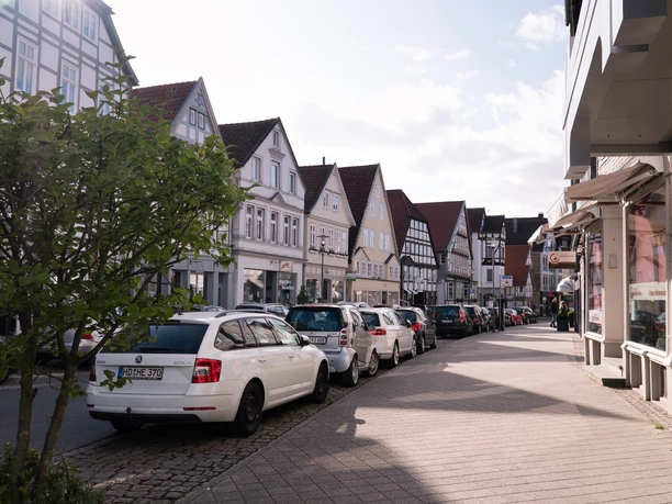 Krumme Straße Straßenansicht mit parkenden Autos und traditionellen Fachwerkhäusern unter wolkigem Himmel.