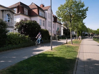 Ein Radfahrer auf einem asphaltierten Weg neben dem Friedrichstaler Kanal, umgeben von Bäumen und Häusern.