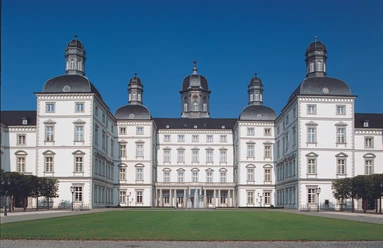 Ein historisches Schloss mit vier Türmen, symmetrischer Fassade und gepflegtem Rasen im Vordergrund.