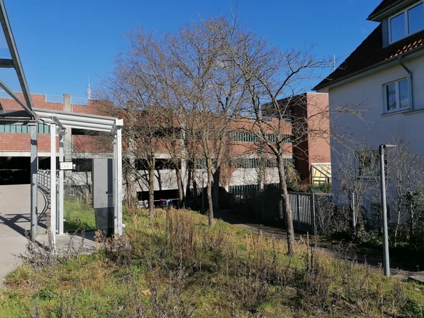 Öffentliche Toilette im Parkhaus nahe dem Hafen, umgeben von Bäumen und Gebäuden in urbanem Umfeld.