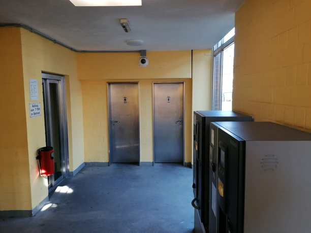WC Parkhaus am Hafen Zwei geschlossene Stahltüren in gelb gestrichenem Flurbereich eines Parkhauses, Kamera und Ticketautomaten.