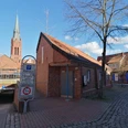 Rote Backstein-Toilettenanlage in der Nähe des Rathauses, mit Zugang zur Tiefgarage und Kirchturm im Hintergrund.