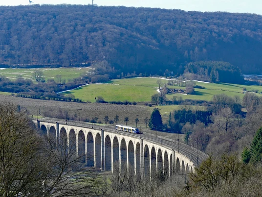 Das Eisenbahnviadukt Altenbeken mit einer vorbeifahrenden Regionalbahn, eingebettet in hügelige Landschaft.