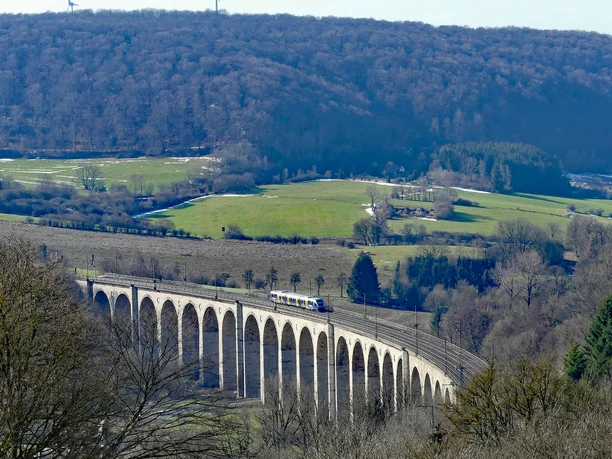 Das Eisenbahnviadukt Altenbeken mit einer vorbeifahrenden Regionalbahn, eingebettet in hügelige Landschaft.