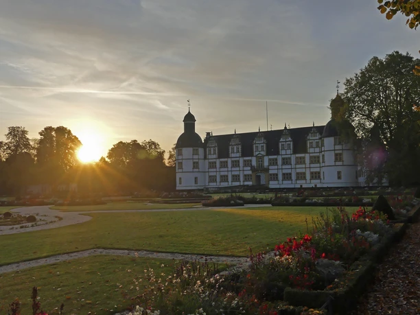 Schloß Neuhaus mit Sonnenaufgang Schloß Neuhaus erhebt sich majestätisch, während die ersten Sonnenstrahlen den Park sanft beleuchten.