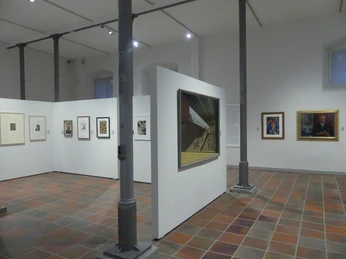 Geräumiger Ausstellungsraum mit modernen Kunstwerken an weißen Wänden, unterstützt von Stahlpfeilern.