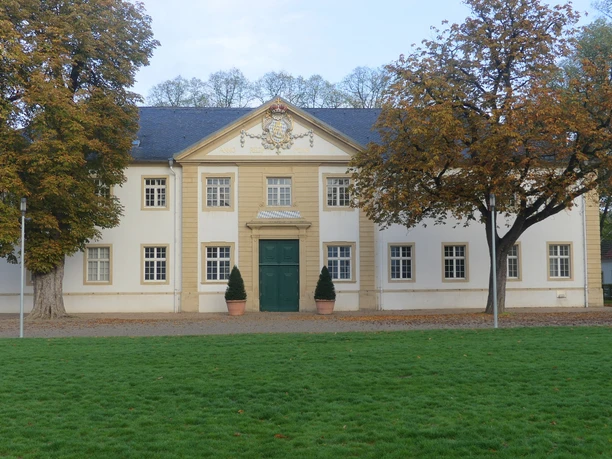 Ehemaliger Marstall (Teilansicht) Ehemaliger Marstall mit weißer Fassade und grünem Tor, flankiert von Herbstbäumen auf Rasenfläche.