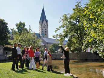Paderquellen Paderborn (Gästeführung) Eine Gästeführerin erklärt einer Gruppe die Paderquellen in Paderborn, im Hintergrund ein Kirchturm.