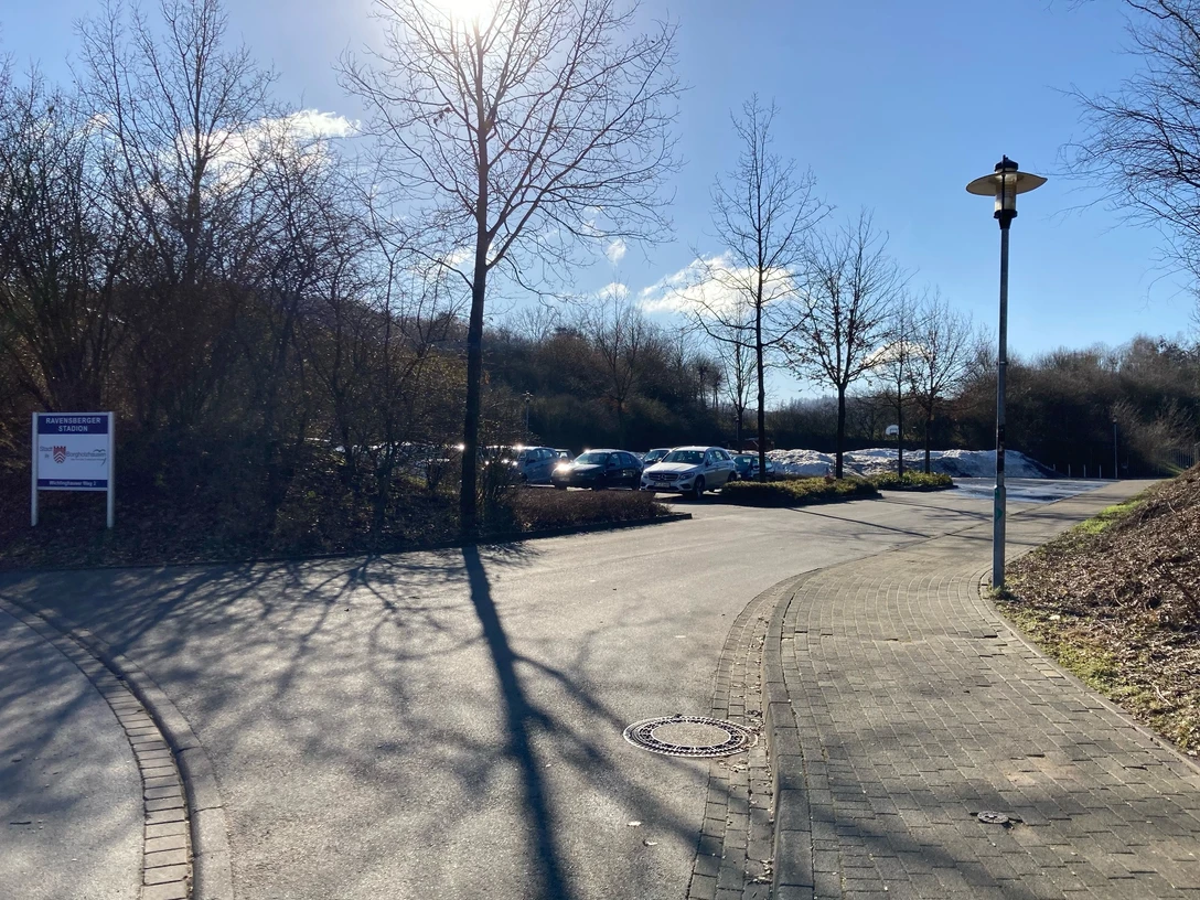 image Gepflasterter Weg mit Straßenlaterne führt zu einem Parkplatz, Bäume und blauer Himmel im Hintergrund.