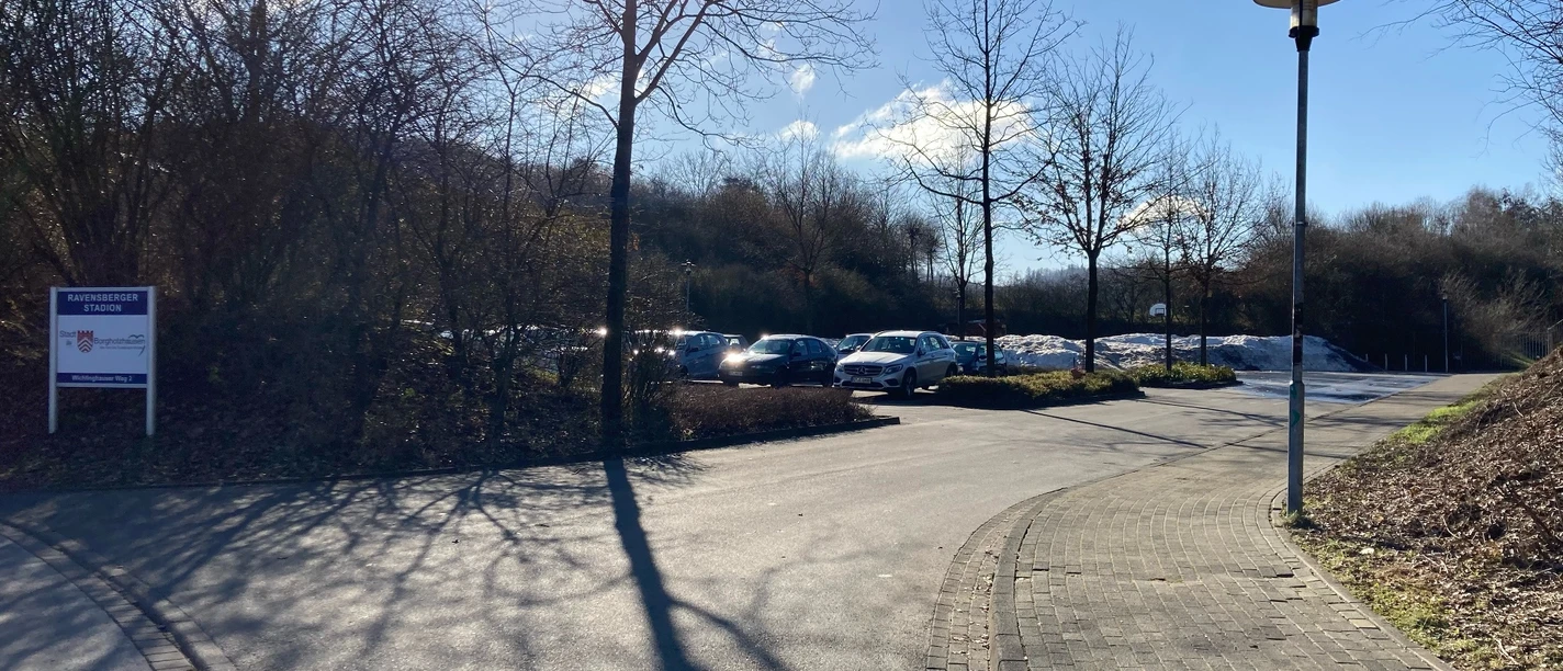 image Gepflasterter Weg mit Straßenlaterne führt zu einem Parkplatz, Bäume und blauer Himmel im Hintergrund.