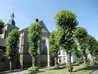 Kirche St. Severin im Ortskern St. Severin Kirche in Lindlar, umgeben von gepflegten Bäumen und blühenden Rasenflächen.