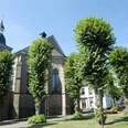 Kirche St. Severin im Ortskern St. Severin Kirche in Lindlar, umgeben von gepflegten Bäumen und blühenden Rasenflächen.