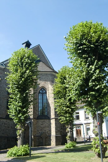 Kirche St. Severin im Ortskern St. Severin Kirche in Lindlar, umgeben von gepflegten Bäumen und blühenden Rasenflächen.