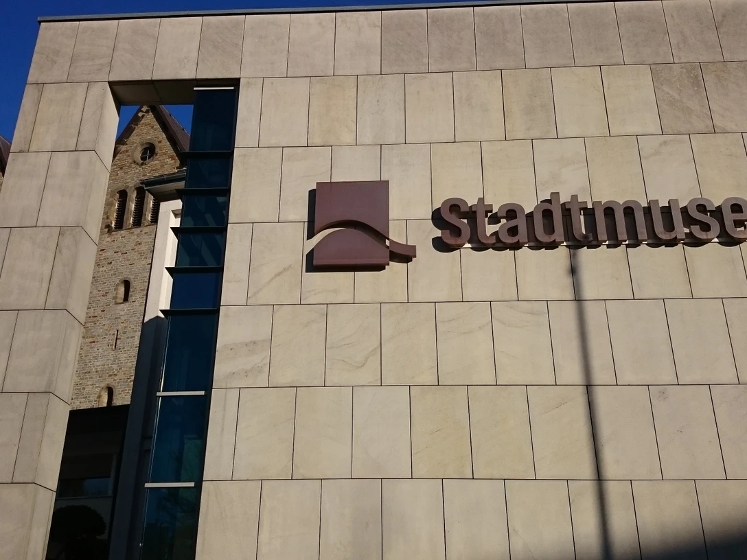 Moderne Fassade des Stadtmuseums Paderborn mit Blick auf die historische Abdinghofkirche im Hintergrund.