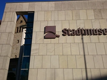 Moderne Fassade des Stadtmuseums Paderborn mit Blick auf die historische Abdinghofkirche im Hintergrund.