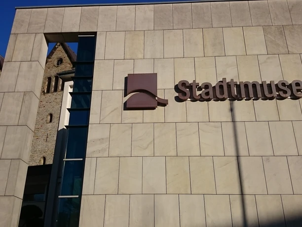 Moderne Fassade des Stadtmuseums Paderborn mit Blick auf die historische Abdinghofkirche im Hintergrund.