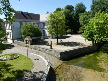 Stadtbibliothek und Quellbecken der Dielenpader Historische Stadtbibliothek in Paderborn neben klarem Quellbecken der Dielenpader, von Bäumen umgeben.