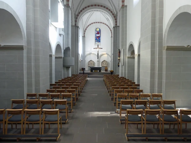 Blick in den Kirchensaal der Gaukirche mit modernen Holzbänken, Altar und buntem Glasfenster.