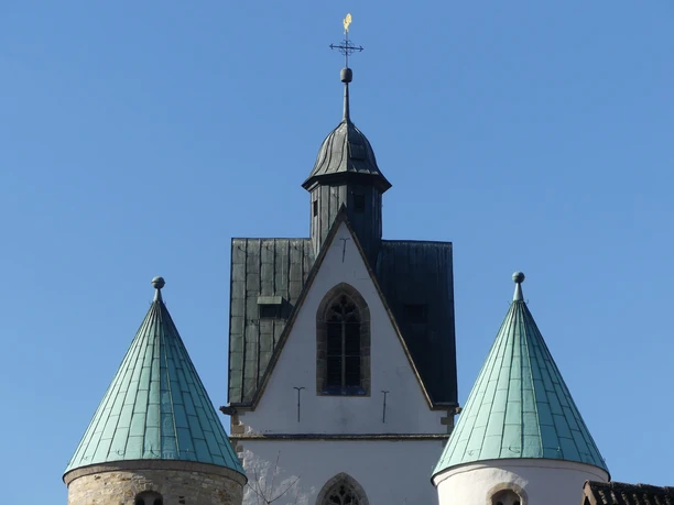 Drei türkisfarbene Kupferdächer der Busdorfkirche in Paderborn ragen vor strahlend blauem Himmel auf.