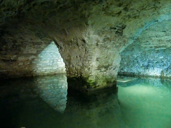 Quellkeller in der Kaiserpfalz Gewölbekeller mit steinernen Bögen und einem Wasserbecken, sanft beleuchtet in kühlem Licht.