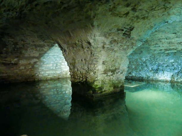 Quellkeller in der Kaiserpfalz Gewölbekeller mit steinernen Bögen und einem Wasserbecken, sanft beleuchtet in kühlem Licht.