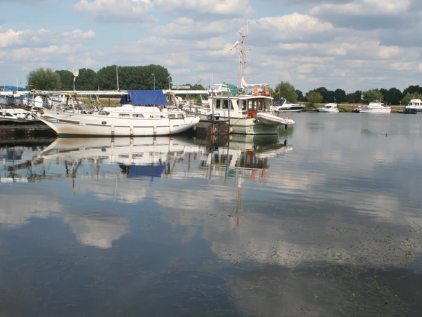 Boats are moored picturesquely in the calm waters of the Mehlbergen Marina, surrounded by a cloudy sky.