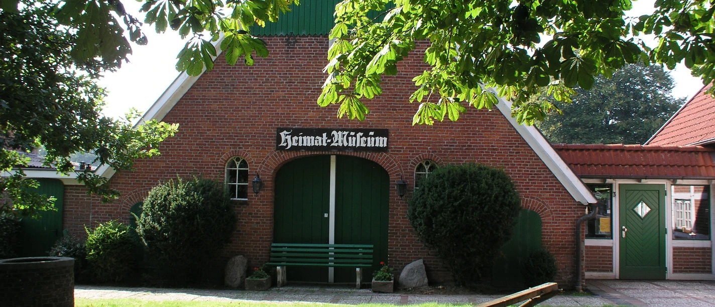 Wanna Heimatmuseum Einladendes Heimatmuseum Wanna: Roter Backsteinbau mit großen grünen Toren unter alten Bäumen.