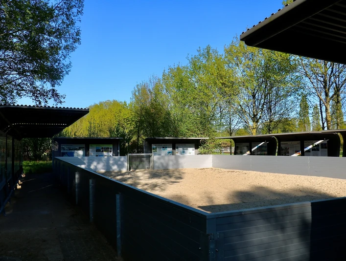 Beach-Soccer-Feld im Parkteil Nord Ein eingezäunter Sandbereich unter freiem Himmel mit mehreren überdachten Pferdeboxen im Hintergrund.