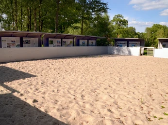 Ein sonniger Sandplatz umgeben von Bäumen und Infotafeln in einem ruhigen Naturpark.