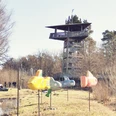 Blick auf den Aussichtsturm im Gartenschaupark Rietberg Holzbeobachtungsturm in Naturpark, umgeben von Bäumen, mit bunten Spielzeugflugzeugen im Vordergrund.