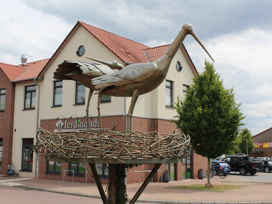 Skulptur Storchennest am Kreisel Petershagen Metallskulptur eines Storchenpaars in einem Nest auf einem Kreisel vor einem Gebäude in Petershagen.