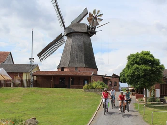 Büschings Mühle Radfahrer erkunden Büschings Mühle, eine historische Windmühle, umgeben von ländlicher Umgebung.