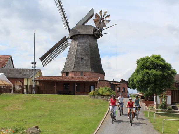 Büschings Mühle Radfahrer erkunden Büschings Mühle, eine historische Windmühle, umgeben von ländlicher Umgebung.