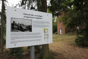 Flakturm des ehem. "Fliegerhorst Plantlünne" Informationstafel zum Flakturm des ehemaligen Fliegerhorsts Plantlünne vor rotem Backsteingebäude.