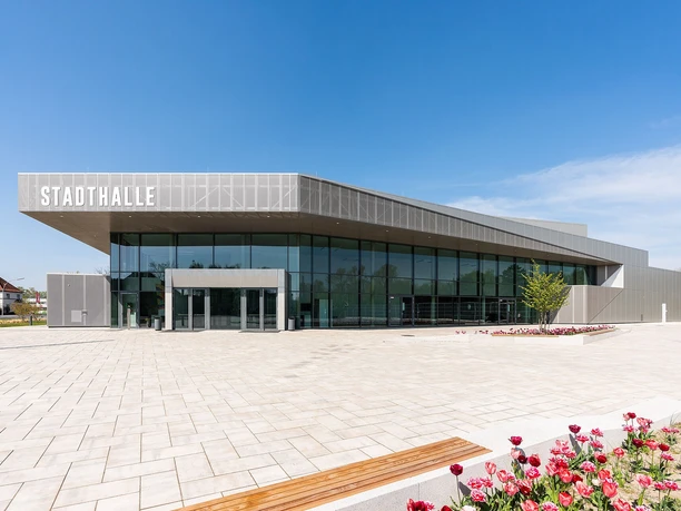 Stadthalle Rheda-Wiedenbrück Moderne Stadthalle in elegantem Grau, umgeben von gepflastertem Platz und blühenden Tulpenbeeten.