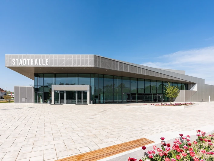 Stadthalle Rheda-Wiedenbrück Moderne Stadthalle in elegantem Grau, umgeben von gepflastertem Platz und blühenden Tulpenbeeten.