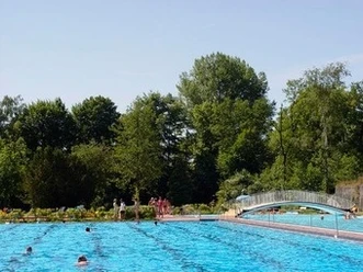 Freibad Wiedenbrück Ein Freibad mit einem großen, blau schimmernden Becken, umgeben von üppigen Bäumen und einer Brücke.