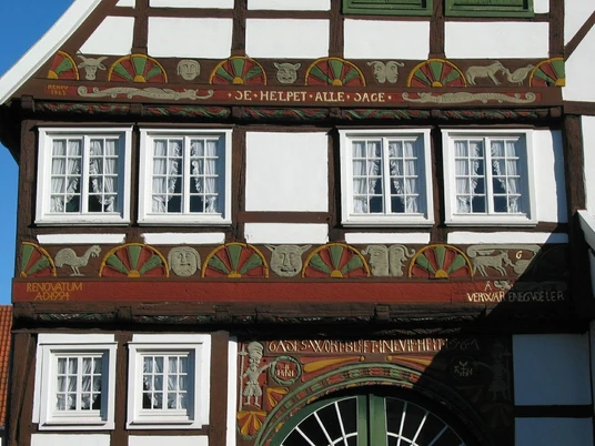 Fachwerkhaus mit reich verzierter Fassade und geschnitzten Holzdetails sowie sechs weißen Fenstern.