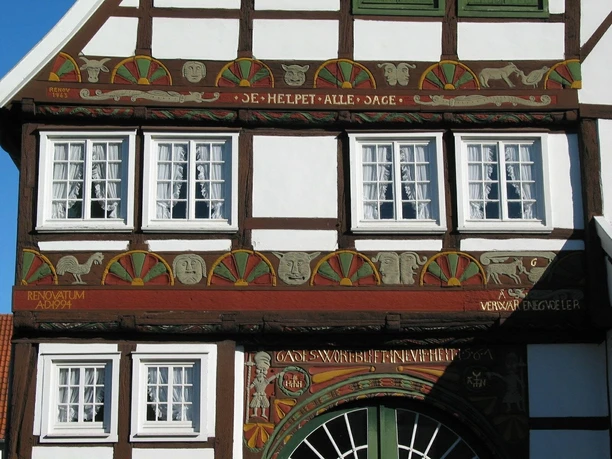 Fachwerkhaus mit reich verzierter Fassade und geschnitzten Holzdetails sowie sechs weißen Fenstern.
