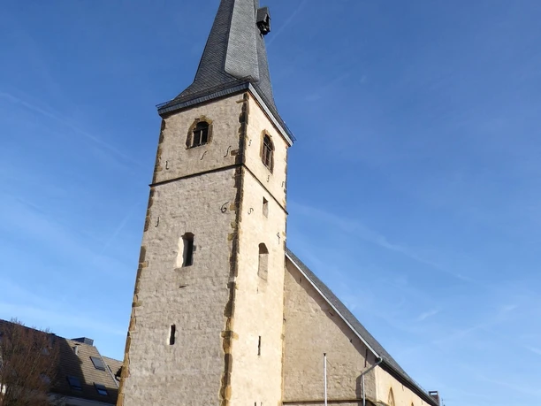 Eine steinerne Kirche mit hohen, spitzen Turm und blauem Himmel in einer ruhigen städtischen Umgebung.