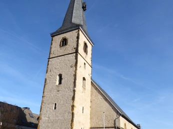 image Eine steinerne Kirche mit hohen, spitzen Turm und blauem Himmel in einer ruhigen städtischen Umgebung.